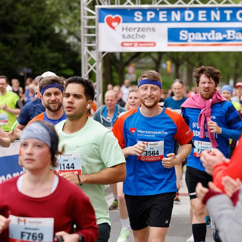 Menschen laufen beim Mainzer Gutenberg Halbmarathon durch das Herzenssache-Spendentor